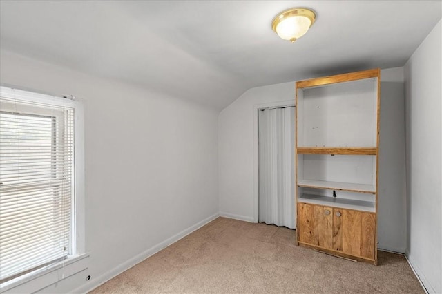 unfurnished bedroom with light colored carpet, multiple windows, lofted ceiling, and a closet