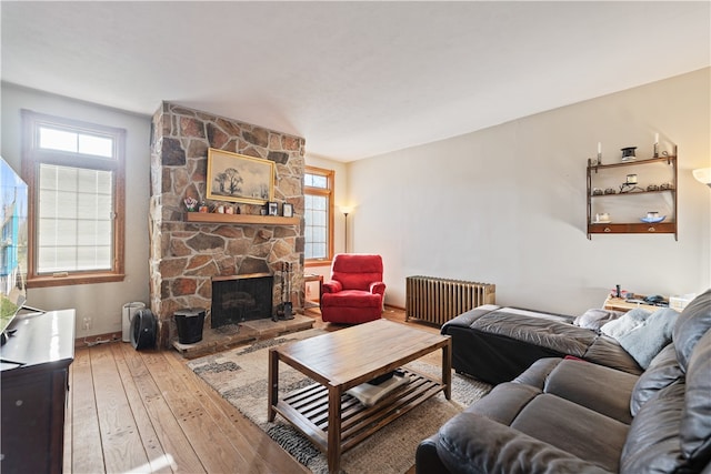 living room featuring a stone fireplace, wood-type flooring, and radiator heating unit