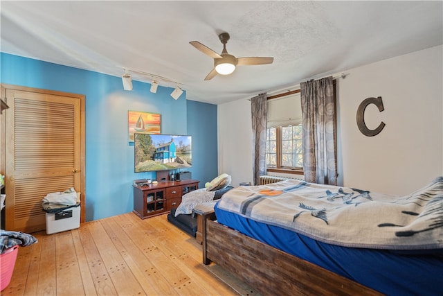 bedroom with a closet, ceiling fan, wood-type flooring, and rail lighting