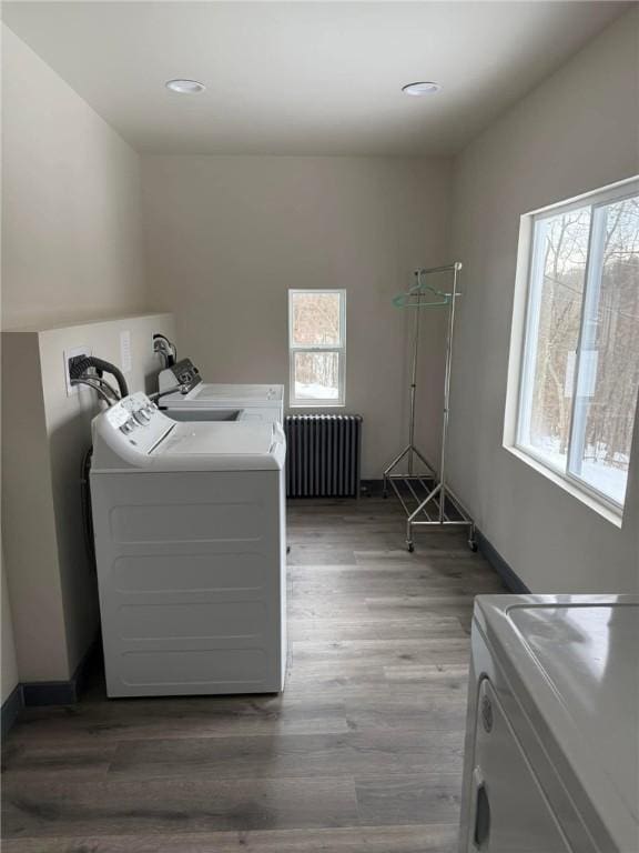 clothes washing area with hardwood / wood-style flooring, independent washer and dryer, radiator, and a wealth of natural light