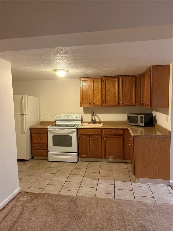 kitchen with sink, light colored carpet, a textured ceiling, and white appliances