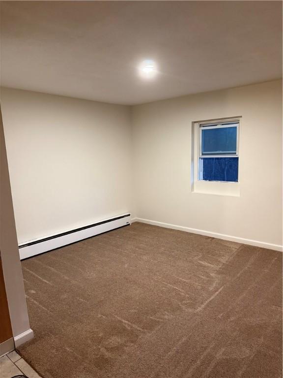 empty room featuring a baseboard heating unit and dark colored carpet