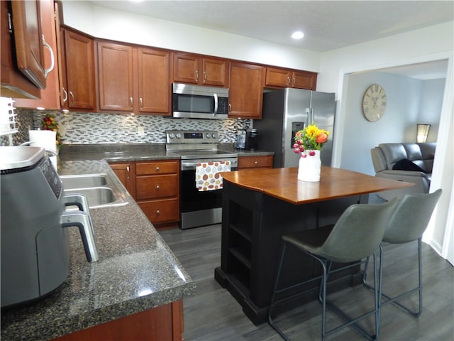 kitchen featuring dark wood-type flooring, decorative backsplash, appliances with stainless steel finishes, a kitchen island, and a kitchen bar