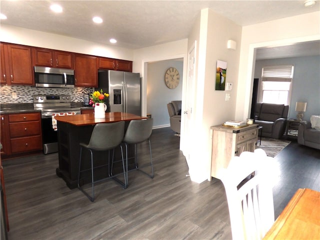 kitchen with a kitchen breakfast bar, backsplash, stainless steel appliances, dark wood-type flooring, and a center island