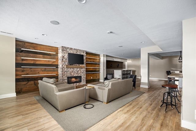 living room featuring wooden walls, a stone fireplace, a textured ceiling, and light wood-type flooring