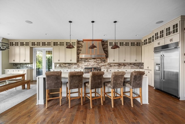 kitchen with wall chimney range hood, dark wood-type flooring, hanging light fixtures, high end appliances, and a center island