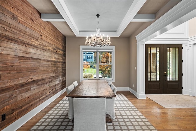 unfurnished dining area with wood walls, light wood-type flooring, french doors, beamed ceiling, and an inviting chandelier