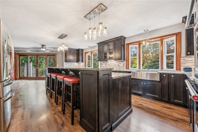 kitchen featuring ceiling fan with notable chandelier, a center island, dark brown cabinetry, dark wood-type flooring, and a breakfast bar