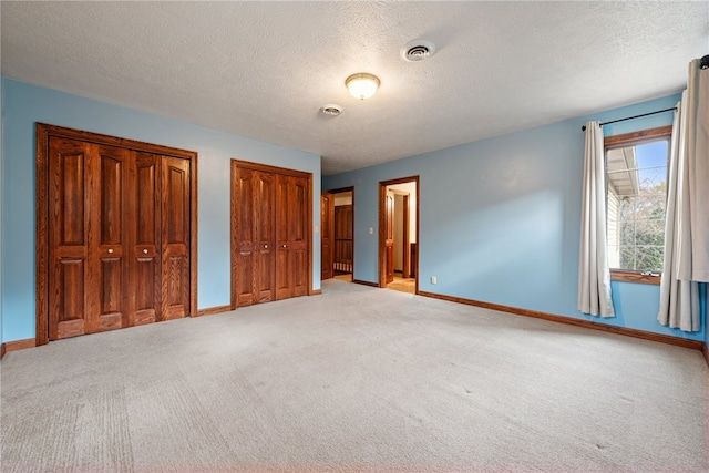 unfurnished bedroom with a textured ceiling, multiple closets, and light colored carpet