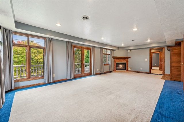 unfurnished living room featuring carpet, a textured ceiling, a healthy amount of sunlight, and french doors