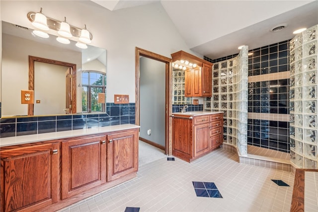 bathroom with decorative backsplash, tile patterned flooring, a shower, vaulted ceiling, and vanity