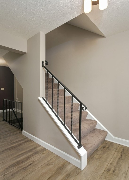 stairway with a textured ceiling and wood-type flooring