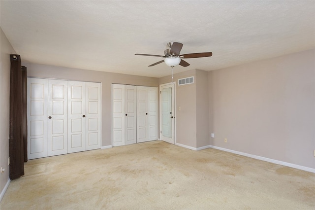 unfurnished bedroom with multiple closets, light carpet, a textured ceiling, and ceiling fan