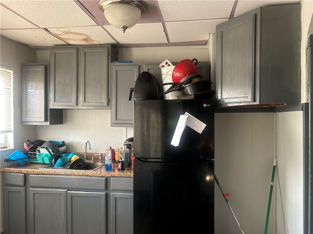 kitchen with gray cabinets, a paneled ceiling, sink, and black refrigerator