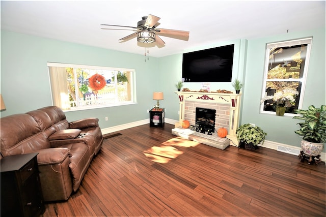 living room with a brick fireplace, ceiling fan, and dark wood-type flooring