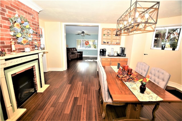 dining room with ceiling fan with notable chandelier, dark hardwood / wood-style flooring, and a brick fireplace