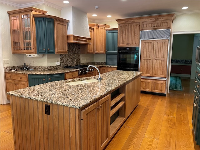 kitchen featuring paneled fridge, crown molding, light hardwood / wood-style flooring, premium range hood, and a kitchen island with sink