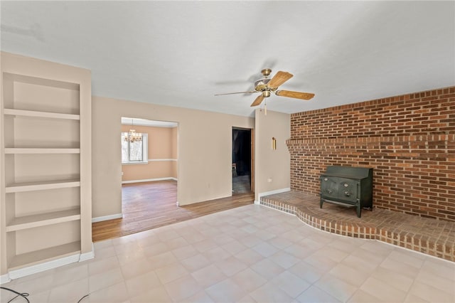 unfurnished living room featuring a wood stove, built in features, ceiling fan with notable chandelier, and light wood-type flooring