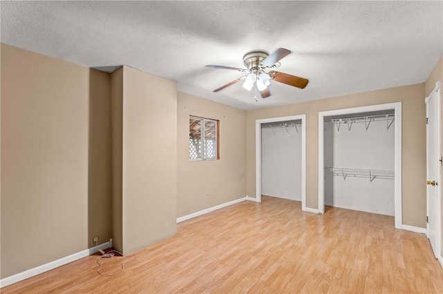 unfurnished bedroom featuring multiple closets, ceiling fan, a textured ceiling, and light wood-type flooring