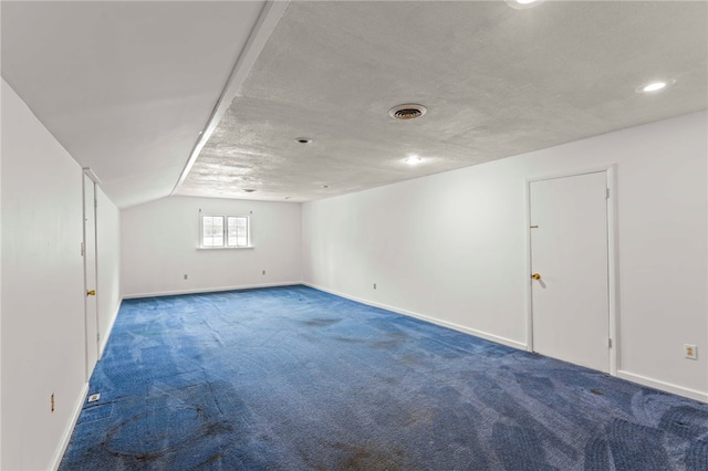 additional living space with a textured ceiling, dark carpet, and lofted ceiling