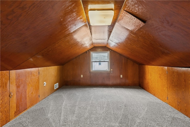 additional living space with wood walls, vaulted ceiling, and light colored carpet