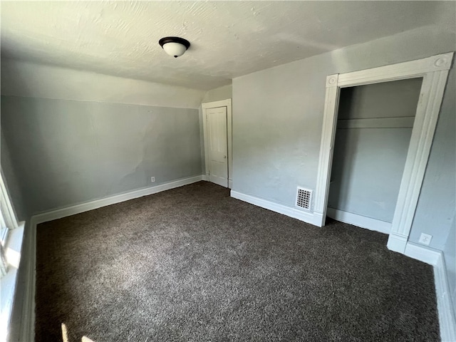 unfurnished bedroom with a closet, a textured ceiling, dark carpet, and vaulted ceiling