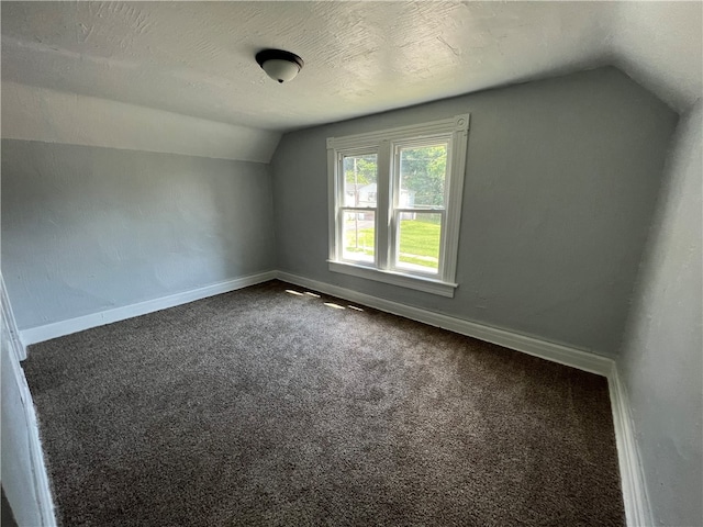 additional living space with a textured ceiling, lofted ceiling, and dark colored carpet