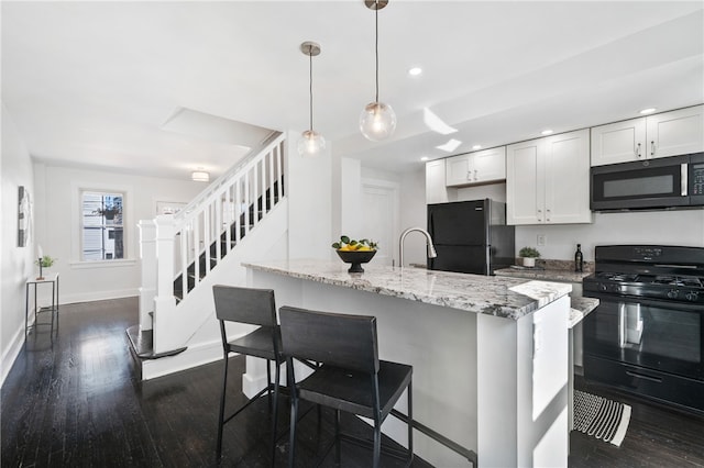 kitchen featuring white cabinets, hanging light fixtures, black appliances, dark wood-type flooring, and light stone counters