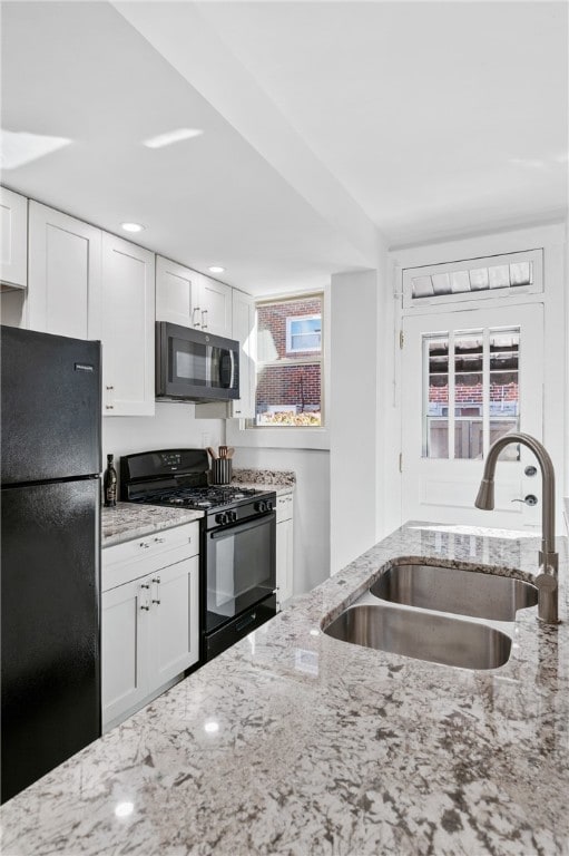 kitchen featuring white cabinets, black appliances, sink, and light stone counters