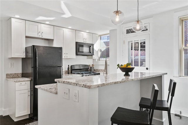 kitchen with black appliances, a kitchen island, white cabinetry, pendant lighting, and light stone counters