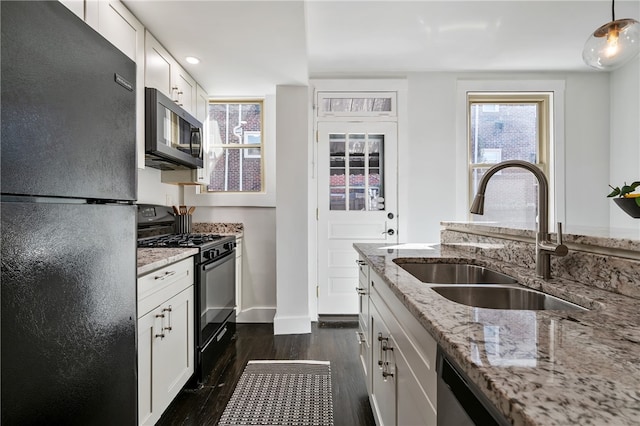 kitchen with hanging light fixtures, sink, light stone countertops, black appliances, and white cabinetry