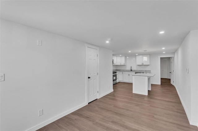 kitchen with decorative backsplash, stainless steel range, a center island, light wood-type flooring, and white cabinetry