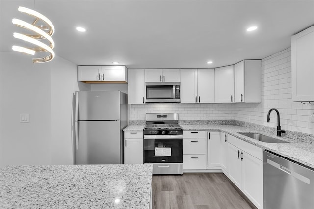 kitchen with white cabinets, sink, pendant lighting, light hardwood / wood-style floors, and stainless steel appliances