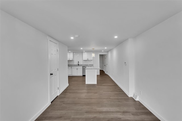 kitchen with wood-type flooring, sink, backsplash, white cabinetry, and stainless steel dishwasher