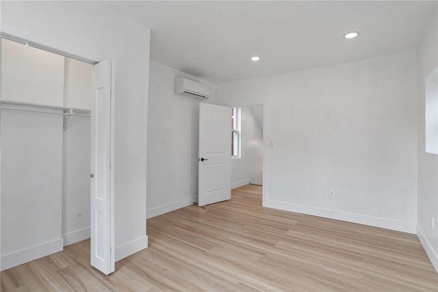 unfurnished bedroom with a closet, a wall mounted AC, and light hardwood / wood-style floors