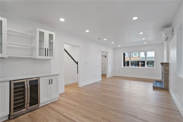 unfurnished living room with light hardwood / wood-style floors, a wall unit AC, and beverage cooler