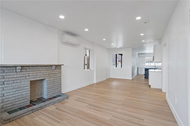 unfurnished living room with an AC wall unit, light hardwood / wood-style flooring, and a brick fireplace