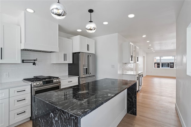 kitchen featuring a kitchen island, stainless steel appliances, dark stone countertops, light wood-type flooring, and white cabinetry