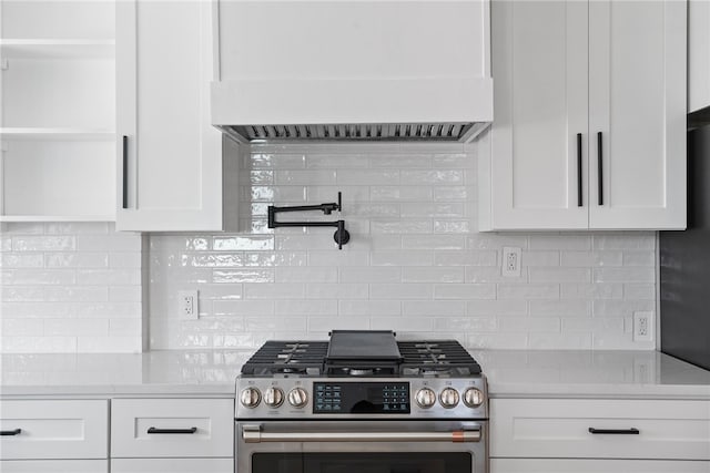 kitchen featuring wall chimney range hood, backsplash, white cabinetry, stainless steel range, and light stone counters