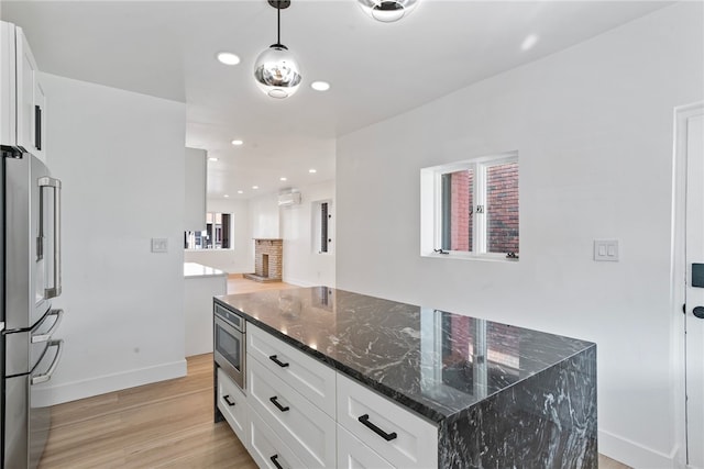 kitchen with appliances with stainless steel finishes, dark stone countertops, white cabinetry, and light hardwood / wood-style floors