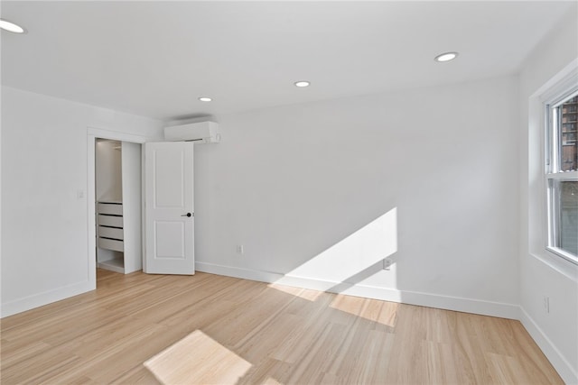 empty room with a wall mounted AC, light hardwood / wood-style floors, and plenty of natural light