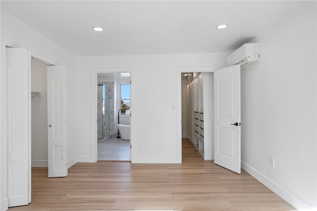 unfurnished bedroom featuring light wood-type flooring, a walk in closet, an AC wall unit, a closet, and connected bathroom