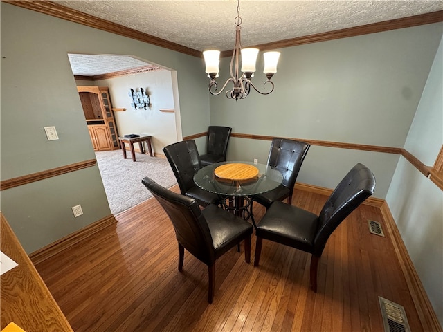 dining room featuring ornamental molding, a textured ceiling, a notable chandelier, and hardwood / wood-style flooring