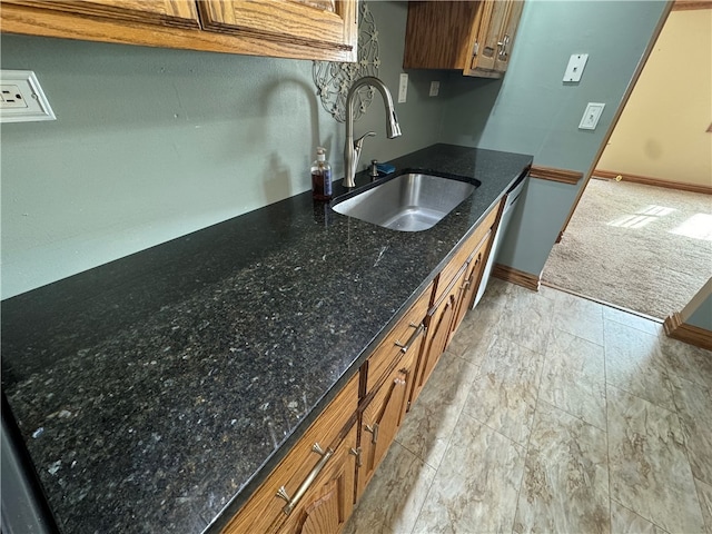 kitchen with stainless steel dishwasher, dark stone countertops, and sink