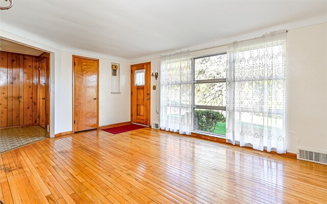 unfurnished living room with wooden walls, wood-type flooring, and plenty of natural light