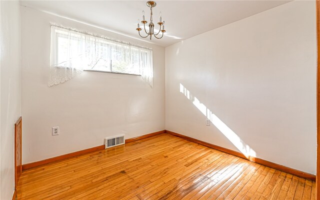 spare room with a chandelier and light wood-type flooring