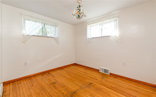 empty room featuring an inviting chandelier, a baseboard radiator, and light wood-type flooring