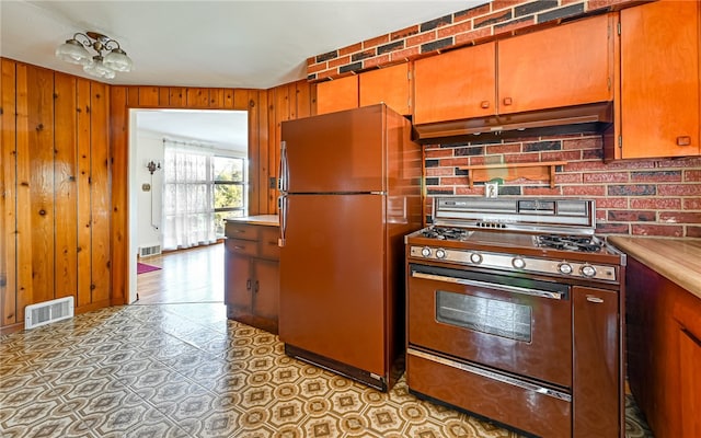 kitchen featuring backsplash, refrigerator, range with gas cooktop, and wood walls