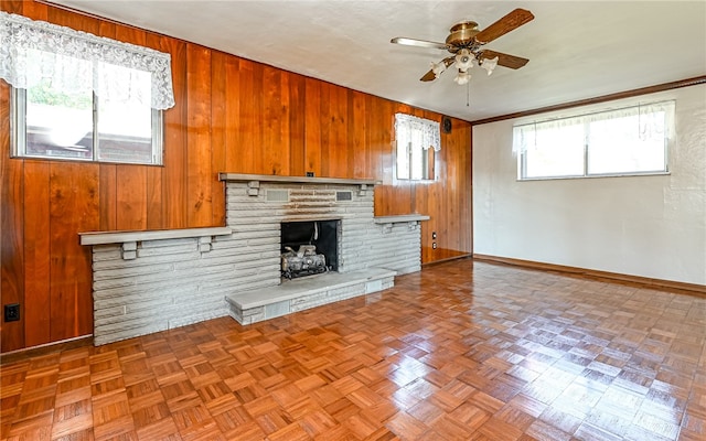 unfurnished living room with wooden walls, parquet flooring, crown molding, a fireplace, and ceiling fan