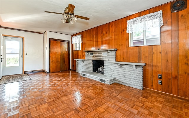 unfurnished living room with wood walls, a healthy amount of sunlight, a fireplace, and ceiling fan